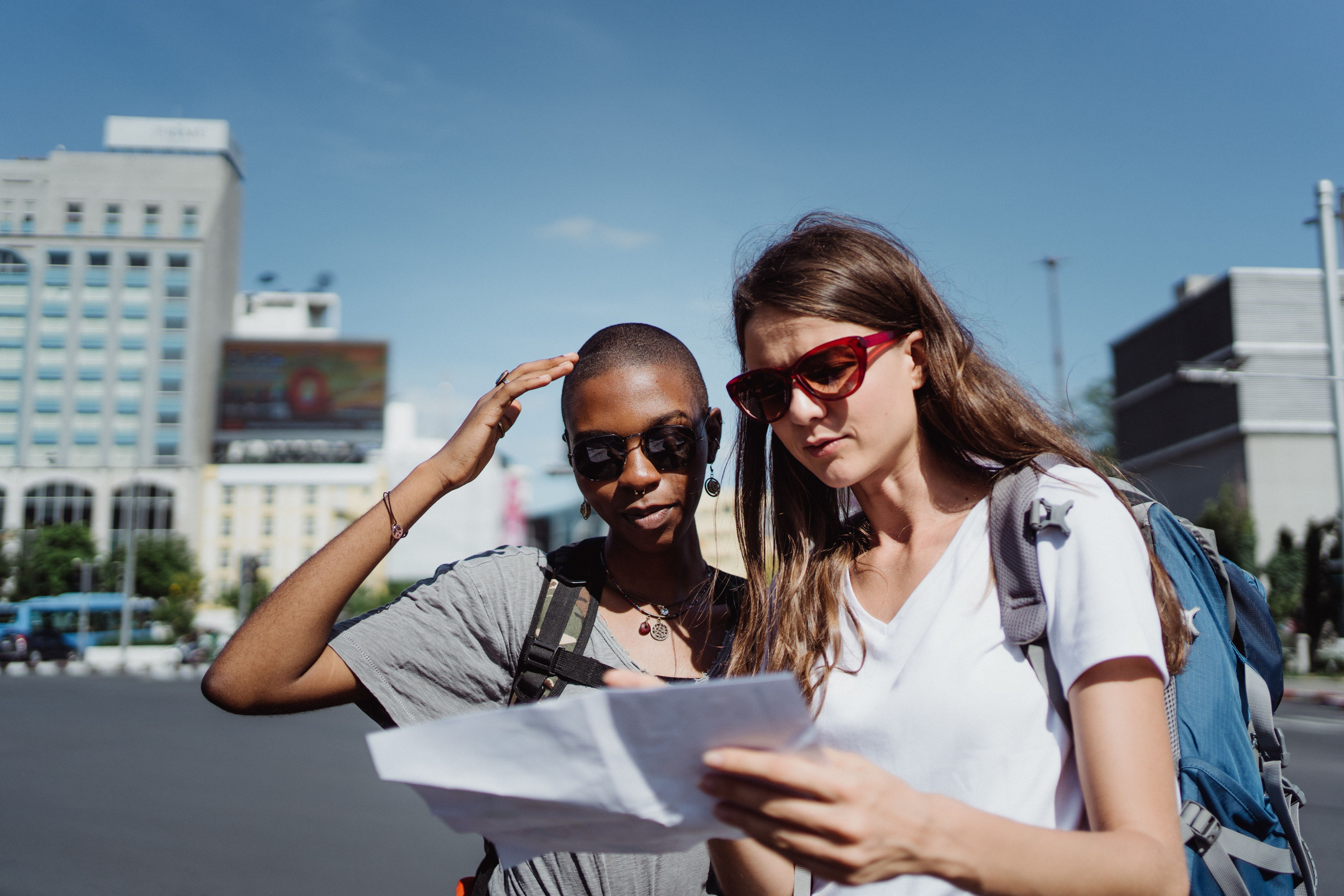 Two travellers in a sunny city square, consulting a map with backpacks on