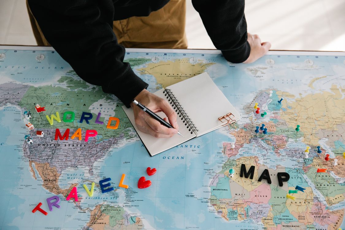 A person writing in a notebook on a world map, planning a travel journey with colorful markers