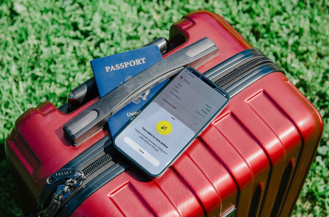 A phone showing an active travel plan resting on a passport and suitcase